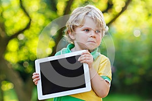 Adorable confused little kid boy holding tablet pc, outdoors