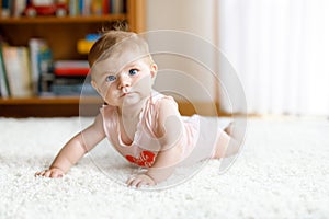 Adorable crawling baby girl`s portrait at home. Little funny girl lifting body and learning to crawl