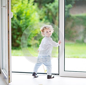 Adorable curly baby girl at big glass door to the garden