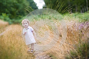 Adorable curly baby girl walking in high grass in autumn park
