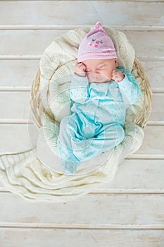 Adorable cute baby girl sleeping in white basket on wooden floor
