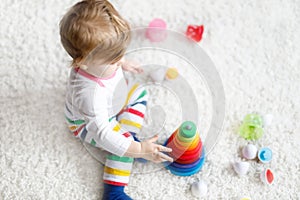 Adorable cute beautiful little baby girl playing with educational colorful wooden rainboy toy pyramid