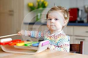 Adorable cute beautiful little baby girl playing with educational wooden music toy at home. Happy excited toddler child