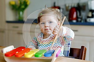 Adorable cute beautiful little baby girl playing with educational wooden music toy at home. Happy excited toddler child