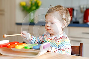 Adorable cute beautiful little baby girl playing with educational wooden music toy at home. Happy excited toddler child