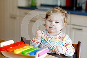 Adorable cute beautiful little baby girl playing with educational wooden music toy at home. Happy excited toddler child