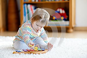 Adorable cute beautiful little baby girl playing with educational wooden music toys at home or nursery. Toddler with