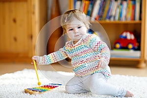 Adorable cute beautiful little baby girl playing with educational wooden music toys at home or nursery. Toddler with