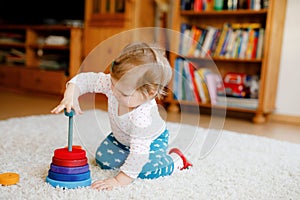 Adorable cute beautiful little baby girl playing with educational wooden toys at home or nursery. Toddler with colorful