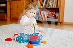 Adorable cute beautiful little baby girl playing with educational wooden toys at home or nursery. Toddler with colorful