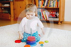 Adorable cute beautiful little baby girl playing with educational wooden toys at home or nursery. Toddler with colorful