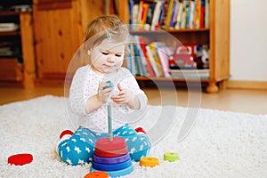 Adorable cute beautiful little baby girl playing with educational wooden toys at home or nursery. Toddler with colorful