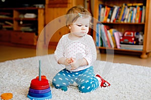 Adorable cute beautiful little baby girl playing with educational wooden toys at home or nursery. Toddler with colorful
