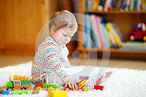 Adorable cute beautiful little baby girl playing with educational wooden toys at home or nursery. Toddler with colorful