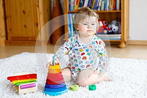 Adorable cute beautiful little baby girl playing with educational wooden toys at home or nursery. Toddler with colorful