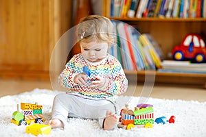 Adorable cute beautiful little baby girl playing with educational wooden toys at home or nursery. Toddler with colorful