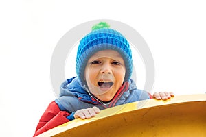 Adorable cute boy playing on playground on a cold day. Child wearing funny hat and red jacket. Funny little boy outdoors. Kids out