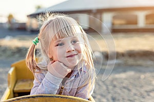 Adorable cute caucasian blond kid girl portrait sitting in wooden cart, looking aside and dreaming at farm or park during warm