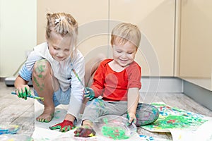 Adorable cute caucasian little blond siblings children enjoy having fun painting with brush and palm at home indoors