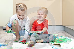 Adorable cute caucasian little blond siblings children enjoy having fun painting with brush and palm at home indoors