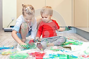 Adorable cute caucasian little blond siblings children enjoy having fun painting with brush and palm at home indoors