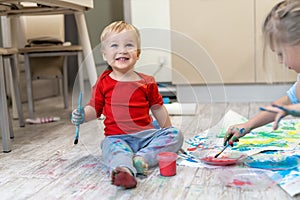 Adorable cute caucasian little blond siblings children enjoy having fun painting with brush and palm at home indoors . Cheerful