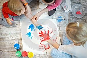 Adorable cute caucasian little blond siblings children enjoy having fun together with mother painting brush and palm at home