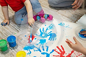 Adorable cute caucasian little blond siblings children enjoy having fun together with mother painting brush and palm at home