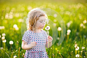 Adorable cute little baby girl blowing on a dandelion flower on the nature in the summer. Happy healthy beautiful