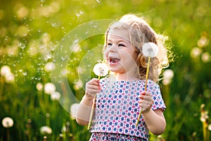 Adorable cute little baby girl blowing on a dandelion flower on the nature in the summer. Happy healthy beautiful