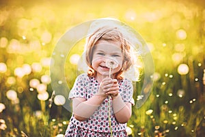 Adorable cute little baby girl blowing on a dandelion flower on the nature in the summer. Happy healthy beautiful