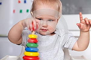 Adorable cute little baby is playing with colorful wooden pyramid