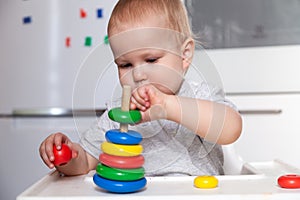 Adorable cute little baby is playing with colorful wooden pyramid