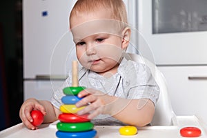 Adorable cute little baby is playing with colorful wooden pyramid