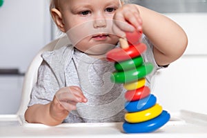 Adorable cute little baby is playing with colorful wooden pyramid