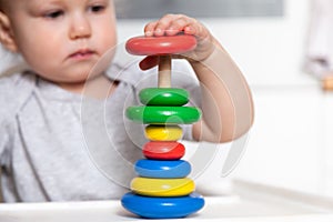 Adorable cute little baby is playing with colorful wooden pyramid. Focus on pyramid