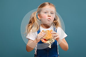 Adorable cute little girl in white shirt and jean jumpsuit with hamburger