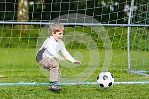 Adorable cute little kid boy playing soccer and football on field