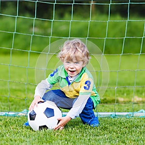 Adorable cute little kid boy playing soccer and football on field