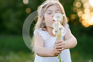 Adorable cute little preschool girl blowing on a dandelion flower on the nature in the summer. Happy healthy beautiful