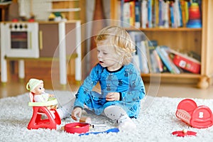 Adorable cute little toddler girl playing with doll. Happy healthy baby child having fun with role game, playing mother at home or