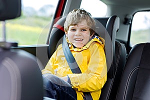 Adorable cute preschool kid boy sitting in car in yellow rain coat.