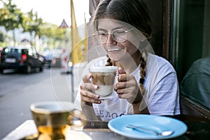 Cute pretty young woman drinks coffee milk foam