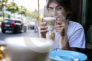 Cute pretty young woman drinks coffee milk foam