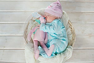 Adorable cute sweet baby girl sleeping in white basket on wooden floor hugging toy tilda rabbits