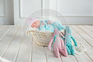 Adorable cute sweet baby girl sleeping in white basket on wooden floor with two toy tilda rabbits