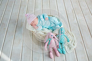 Adorable cute sweet baby girl sleeping in white basket on wooden floor with two toy tilda rabbits