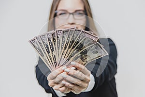 Adorable excited young business woman is showing a pile of money, isolated on white background. Girl is satisfied by