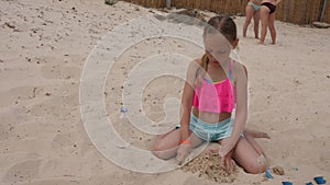 Adorable female child playing with sand and sitting on beach