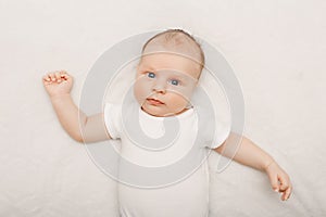 Adorable funny white Caucasian baby with blue grey eyes lying on bed